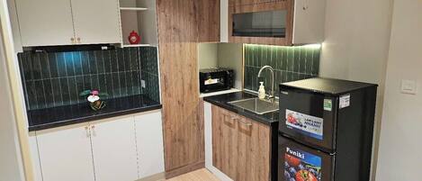 Una cocina con encimera negra, armarios de madera, microondas, refrigerador y pileta.