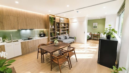 A modern kitchen with wooden cabinets, a dining table with chairs, a refrigerator, and a living area with a sofa and a coffee table.. Joy Apartment Pearl West Lake