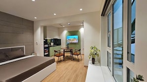 Una habitación moderna con cama, una mesa de comedor con sillas, un televisor y una planta.