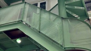 Una estructura de escaleras metálicas verdes de varios niveles, con un árbol al fondo.