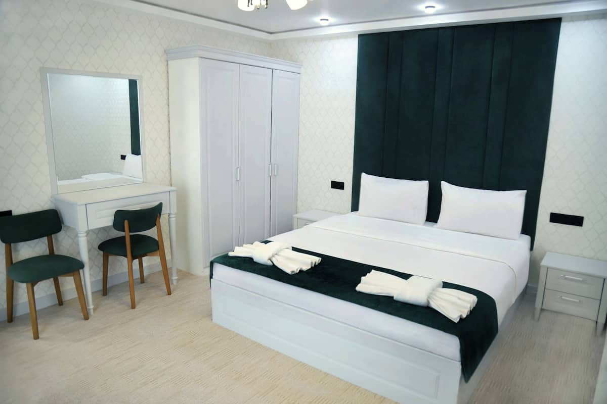 A bedroom with a bed, a desk with chairs, a wardrobe, and a large mirror.