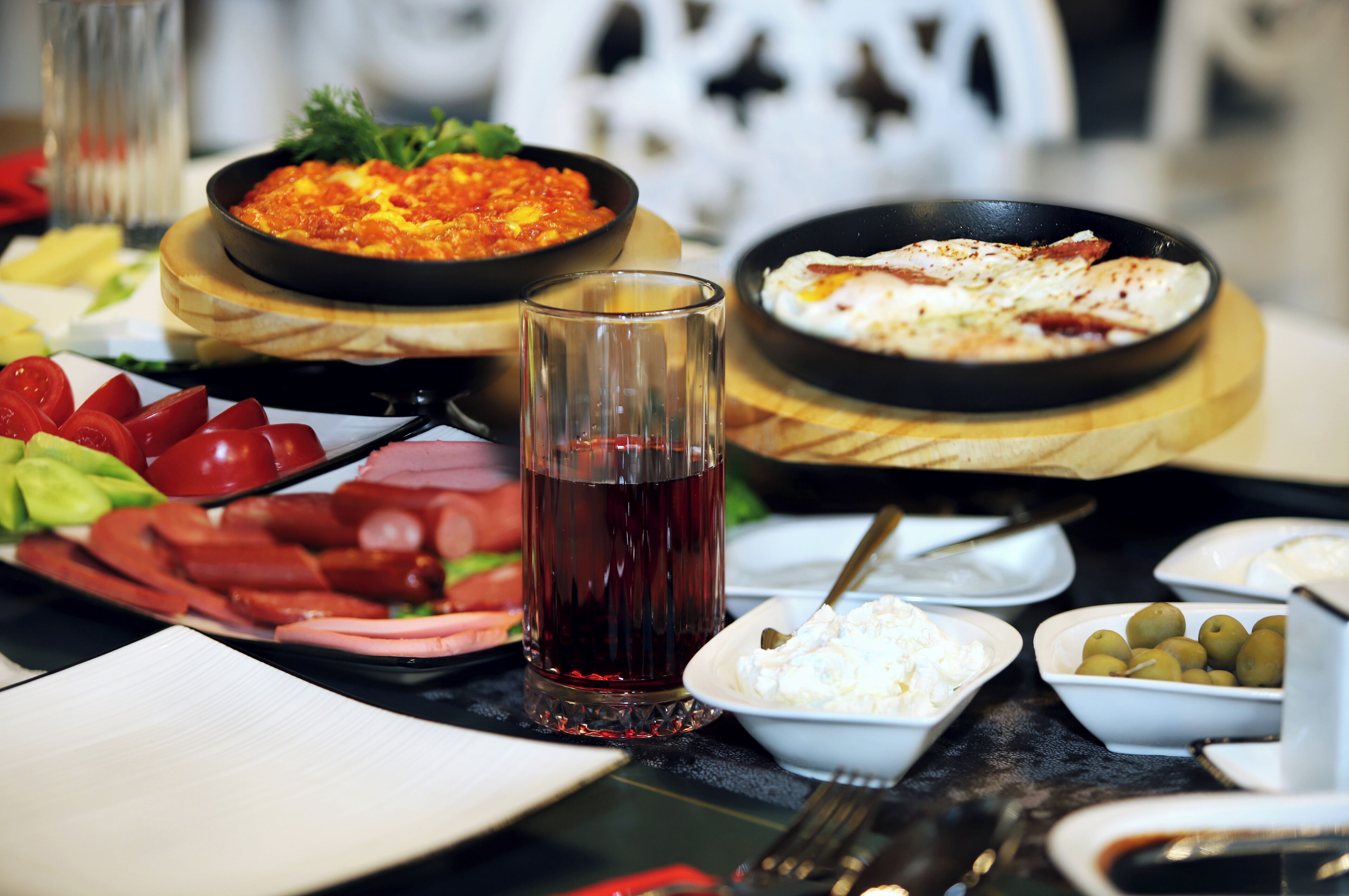 Uma mesa com diversos pratos, um copo de bebida vermelha e pequenas tigelas de azeitonas e queijo.