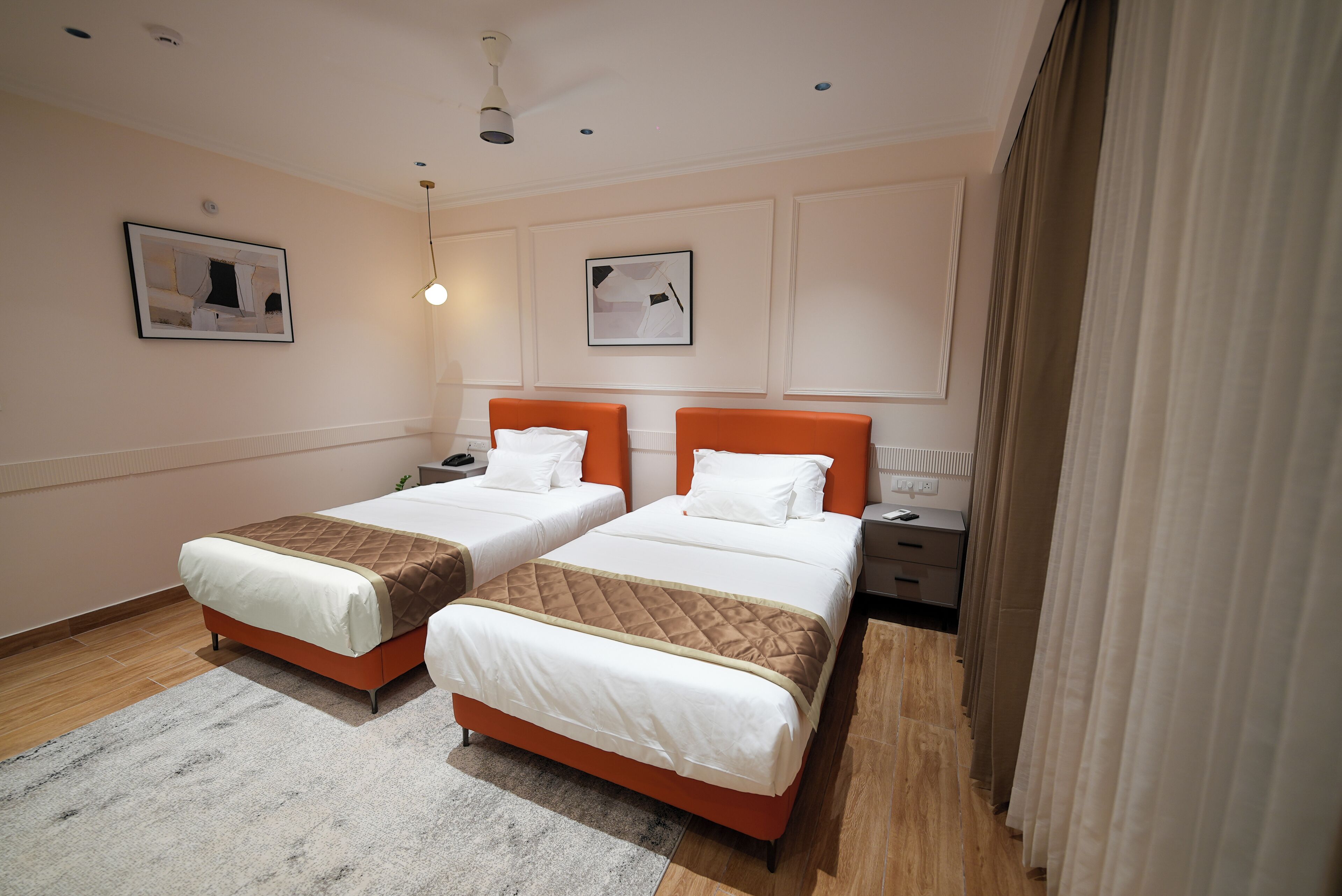 Una habitación de hotel con dos camas, una mesita de noche, una lámpara y una ventana con cortinas.