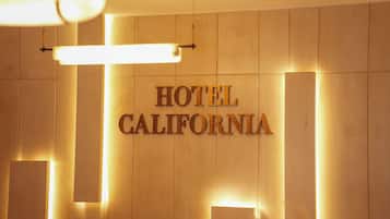 Een muur met de tekst 'HOTEL CALIFORNIA' verlicht door bovenliggende lampen.