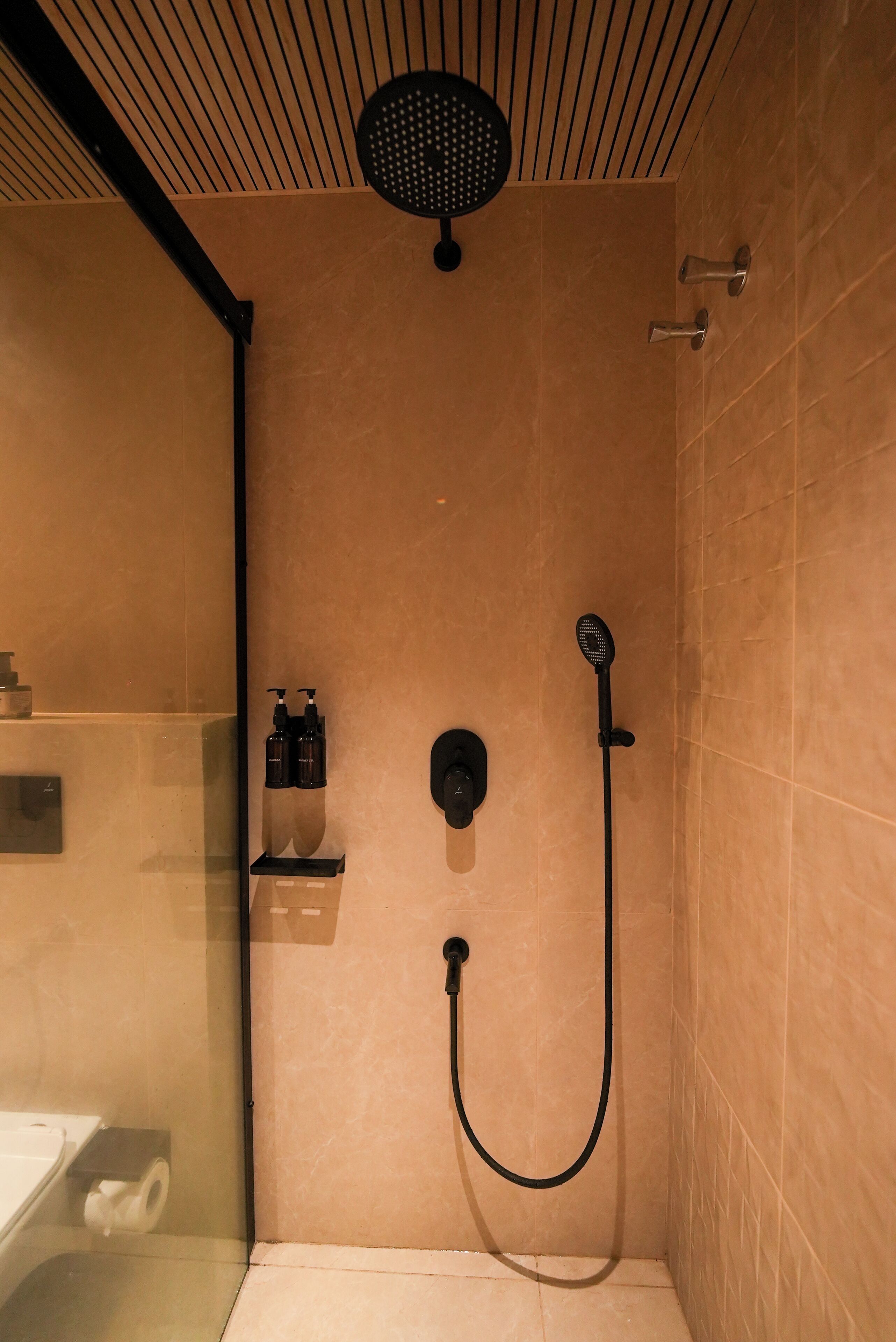 A shower with a handheld showerhead, a wall-mounted faucet, and a glass partition.