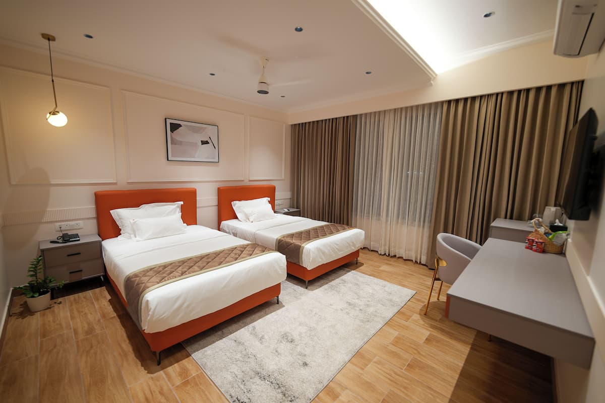 Ein Hotelzimmer mit zwei Betten, einem Schreibtisch, einem Stuhl, einer Topfpflanze und einem Deckenventilator.
