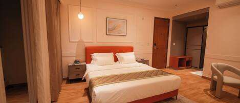 A modern bedroom with a bed, bedside tables, a nightstand, a chair, and a painting on the wall.