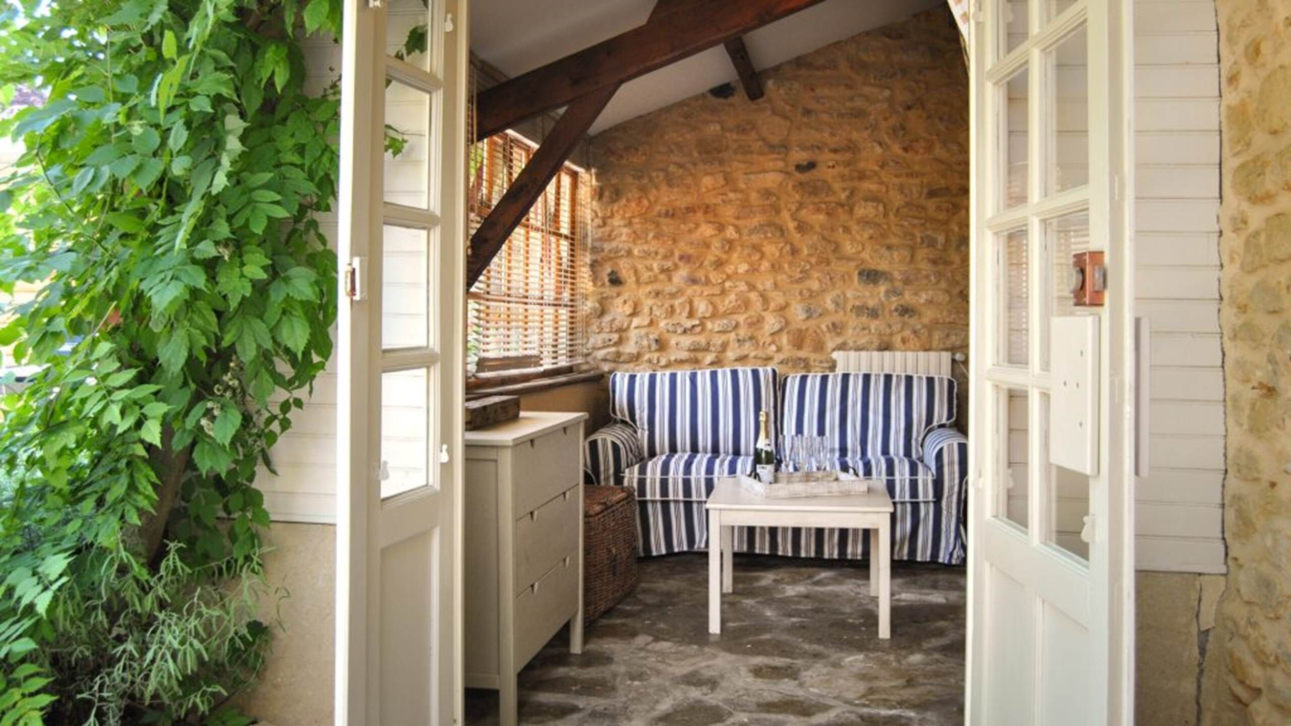 A stone-walled room with a striped sofa and a table, a wooden door, and a plant.