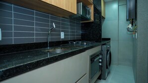 A modern kitchen with a stainless steel sink, a microwave, a stove, and a built-in oven. - Flat Praça do Parnamirim by Easy Home (Recife)