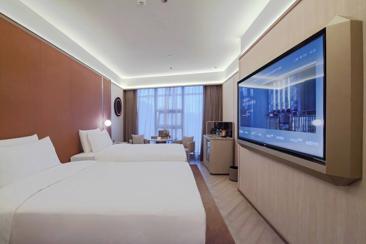 Habitación de hotel con dos camas, un escritorio, un televisor y un ventanal grande.