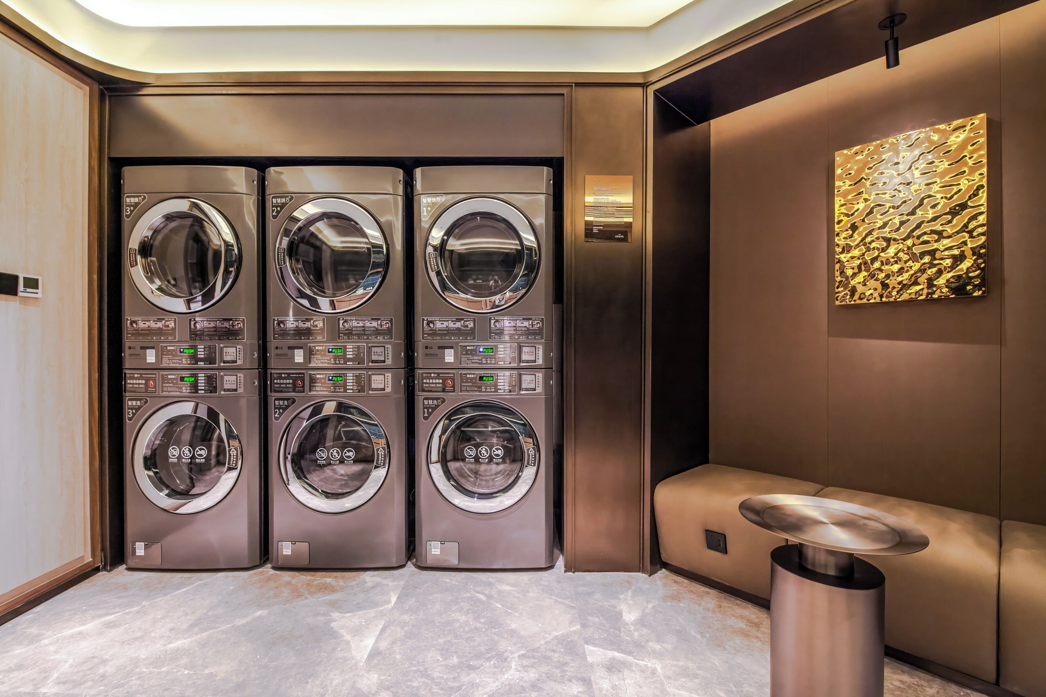 A modern laundry room with four wall-mounted washing machines, a marble floor, a wall-mounted sink, and a textured artwork piece.