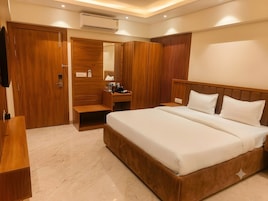 Une chambre d’hôtel avec un grand lit, une armoire en bois, un petit bureau avec une lampe et un appareil de climatisation.
