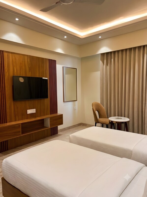 A hotel room with two beds, a TV, a mirror, a chair, a small table, and a ceiling fan. - Sawarthia Sewa Sadan Ayodhya (Faizabad)
