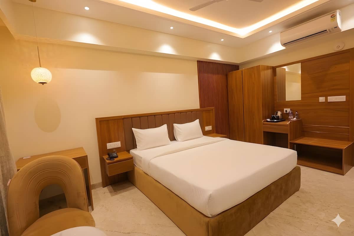 A hotel room with a large bed, wooden headboard, bedside tables, a desk, a chair, a mirror, and an air conditioning unit.
