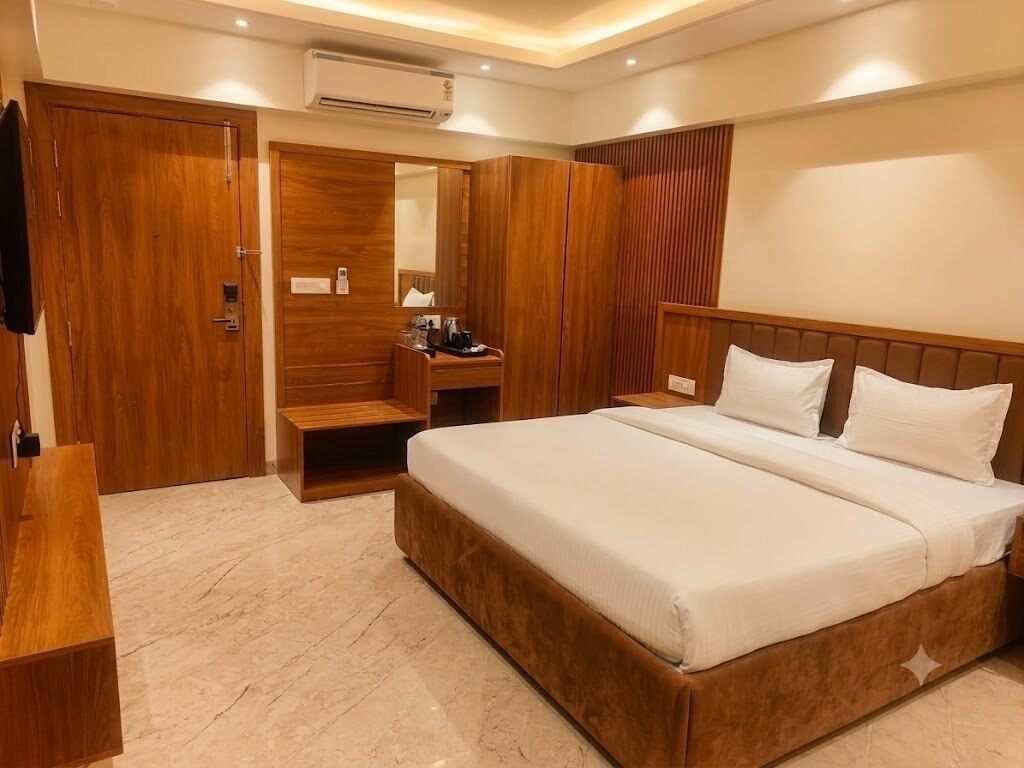 A hotel room with a large bed, wooden wardrobe, a desk with a chair, and a mirror.