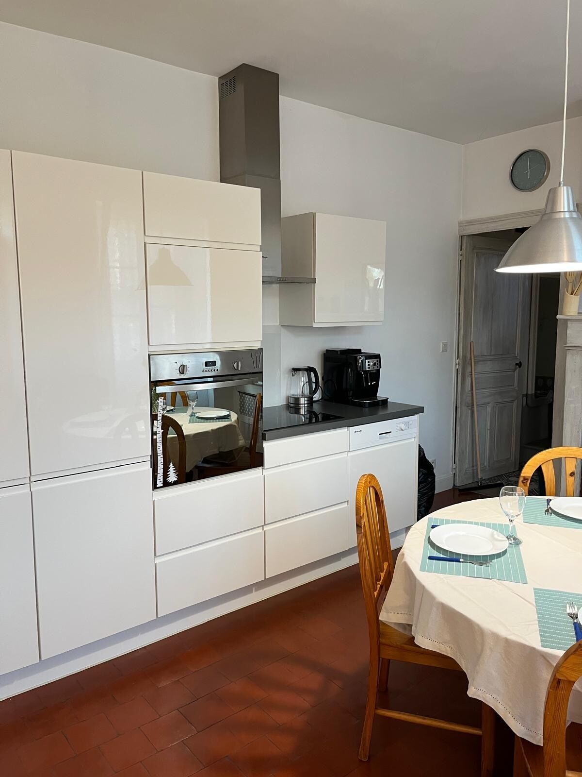 Cocina compacta con armarios blancos, estufa, cafetera y comedor con mesa para dos.
