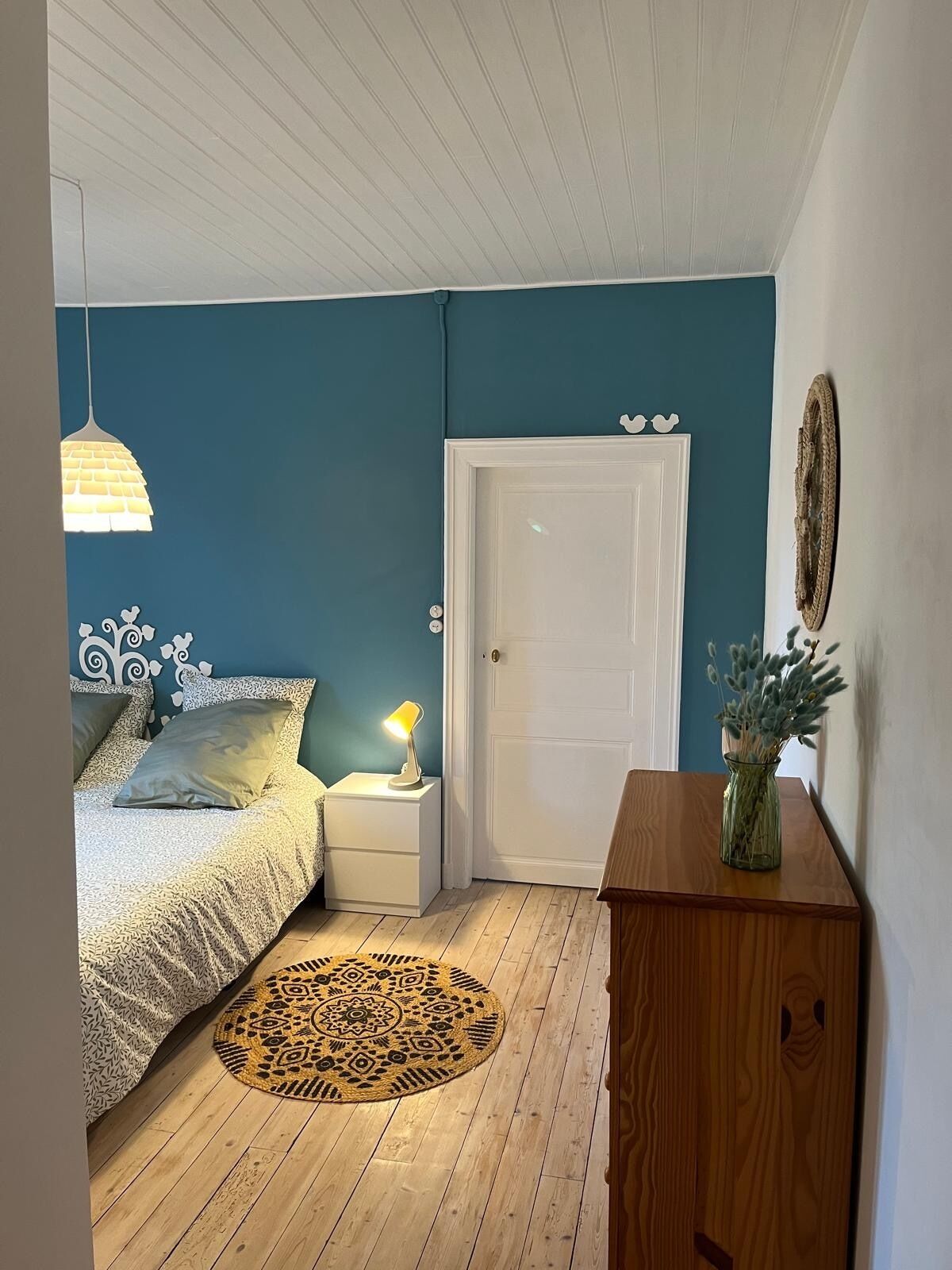 A bedroom with a bed, bedside table, lamp, and a door.
