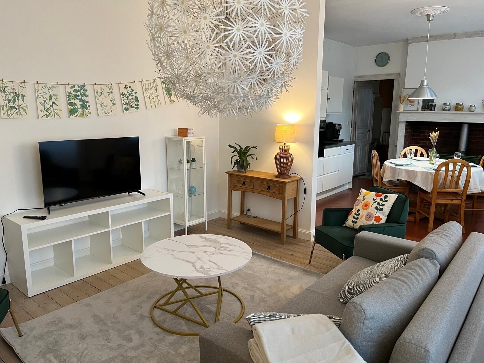 Ett vardagsrum med en TV, ett runt bord i marmor, en soffa, en matplats med bord och stolar, ett kök i bakgrunden och en dekorativ taklampa.