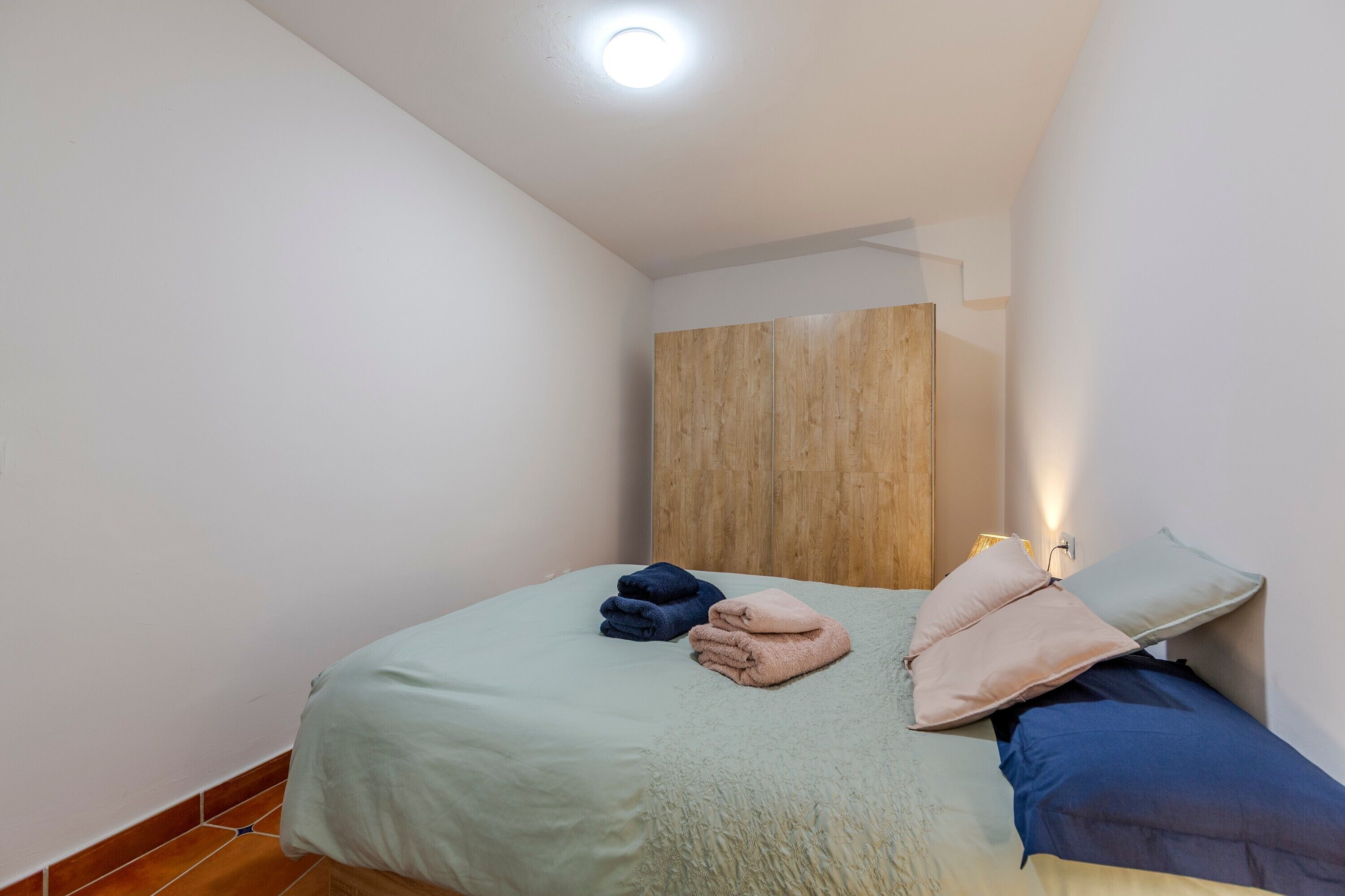 A small, neatly arranged bedroom with a bed, pillows, and folded towels.