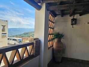 Een balkon met uitzicht op een bus en bergen, een bloempot en een traditionele houten balustrade.