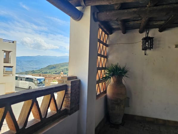 A balcony with a view of a bus and mountains, a potted plant, and a rustic ceiling.