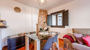 A dining area with a glass table, chairs, a brick fireplace, and a sofa with cushions.