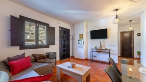 A living room with a sofa, a coffee table, a TV mounted on the wall, and a dining area with chairs and a table.