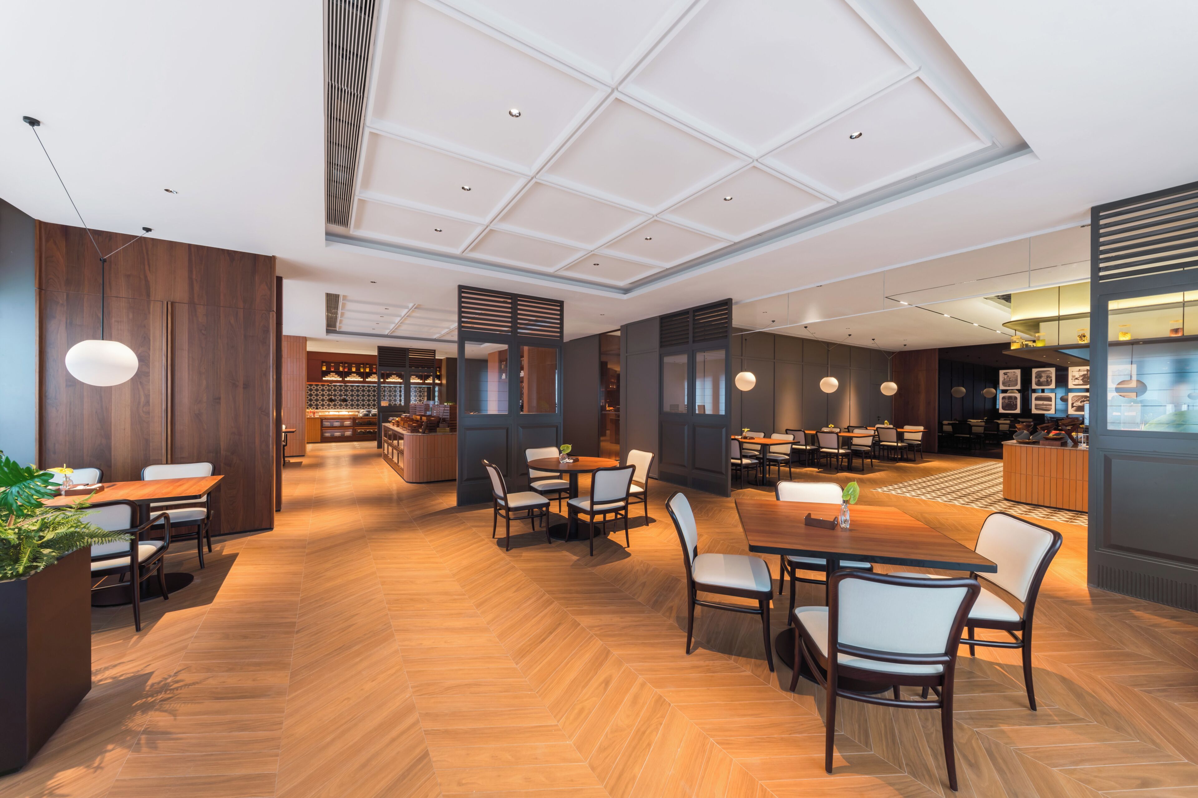 Un restaurant moderne doté d’un plancher en bois, de plusieurs espaces de restauration et d’un éclairage suspendu.