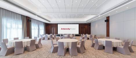 A conference room with round tables and chairs, a large screen displaying 'Intercity Hotel,' and a modern ceiling design.