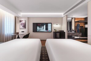 Une chambre d ’hôtel avec deux lits, une télévision, une petite table avec une chaise, un bureau, un miroir et une armoire.