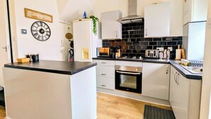 A modern kitchen with white cabinets, a black countertop, a built-in oven, and a black and white backsplash. - Harold House (Leeds)