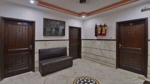 A lobby with three wooden doors, a bench, a framed artwork, and fire extinguishers. - Hotel PG International (New Delhi)