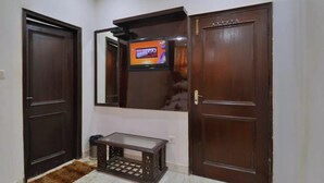 A hallway with two wooden doors, a small table, and a television mounted on the wall. - Hotel PG International (New Delhi)