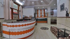A reception area with a curved counter, framed pictures, a fish tank, and patterned seating. - Hotel PG International (New Delhi)