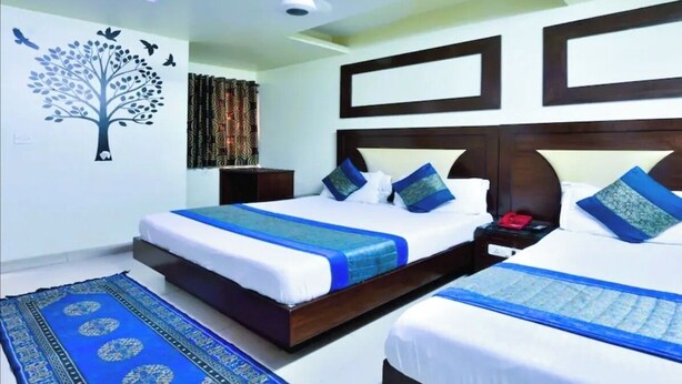 A hotel room with two beds, a ceiling light, a wall mural, and a patterned rug. - Hotel PG International (New Delhi)