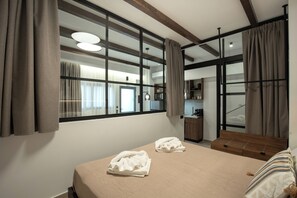 Habitación de hotel con cama, dos toallas, cabecera de madera, ventana con cortinas y un área de kitchenette.