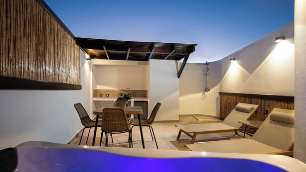 Un espacio moderno al aire libre con jacuzzi, sillones de descanso, una mesa de comedor con sillas y una zona de cocina.