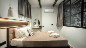 Una habitación de hotel moderna con cama, mesita de noche, espejo, ventana y unidad de aire acondicionado.