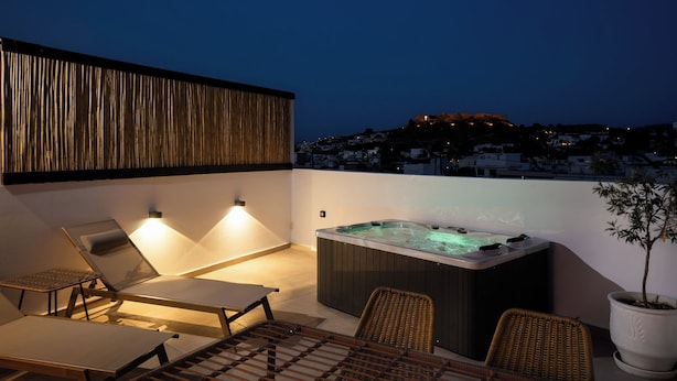 En tagterrasse med jacuzzi, liggestole og udsigt over bybilledet i skumringen.