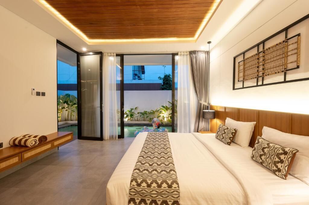 A bedroom with a large bed, a bench, a view of the pool, and a balcony.