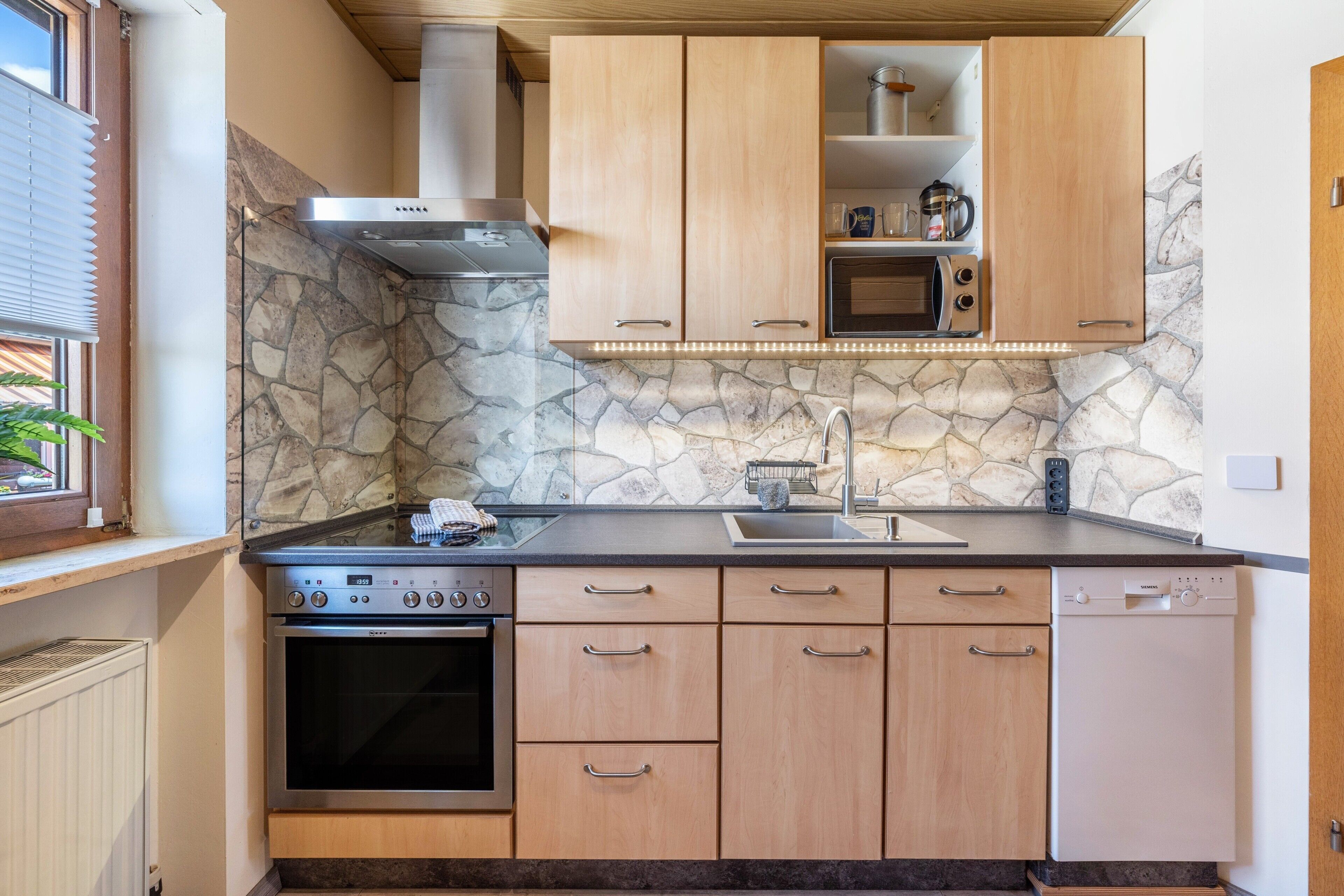 A kitchen with a stone backsplash, wooden cabinets, a built-in microwave, and a dishwasher.