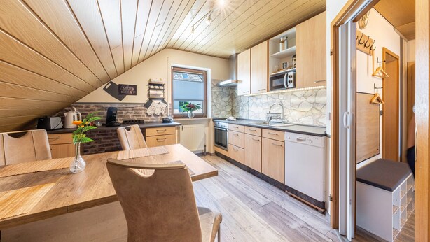 A kitchen with wooden cabinets, a stone backsplash, and a dining area with a table and chairs. - Apartment 'Bassd Scho' with Shared Garden, Balcony and Wi-Fi (Ebensfeld)