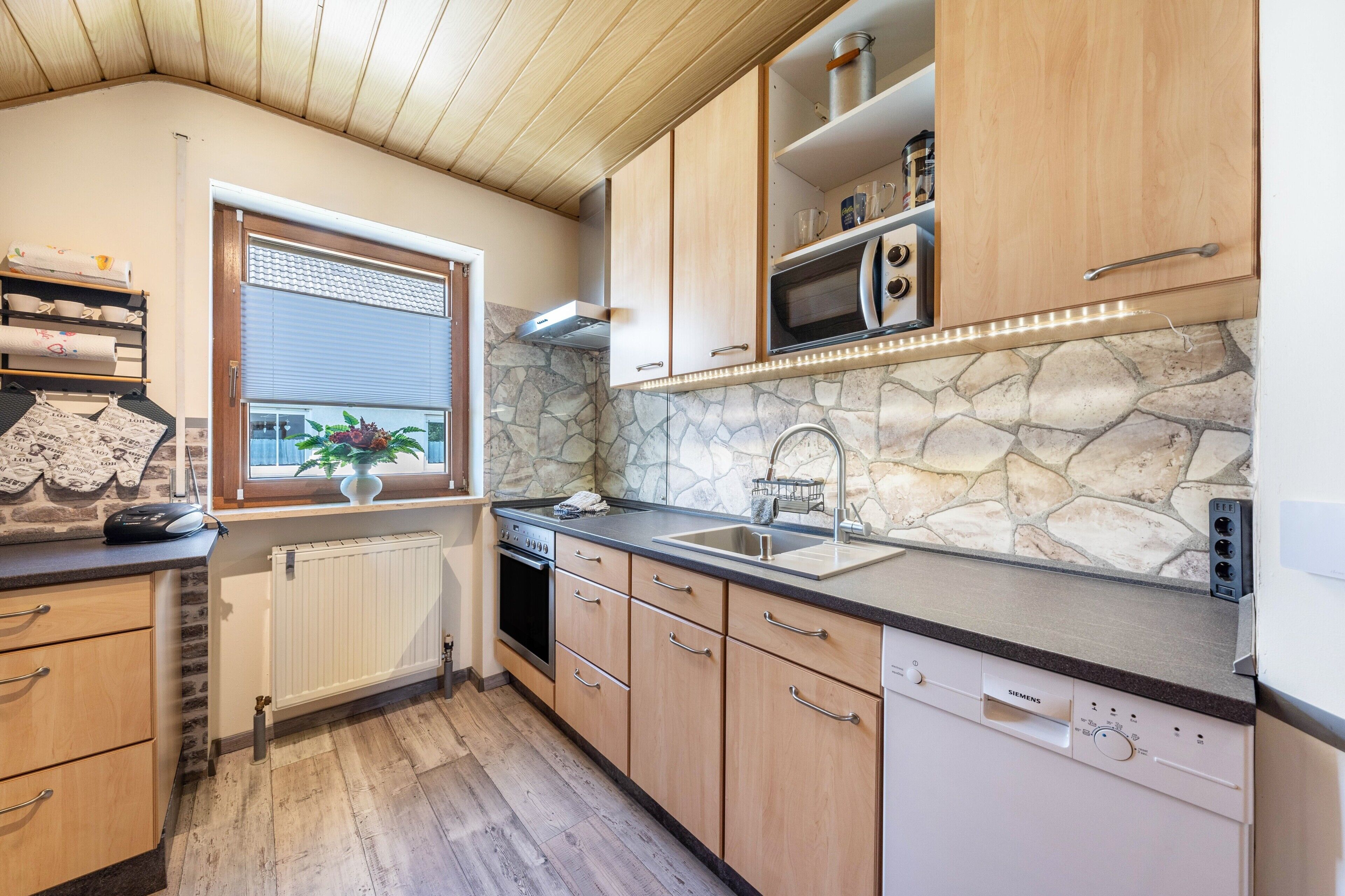 A kitchen with wooden cabinets, a stone backsplash, a built-in oven, and a window with blinds.