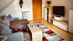A cozy living room with a sofa, a coffee table, a TV, and a wooden cabinet. - Apartment 'Bassd Scho' with Shared Garden, Balcony and Wi-Fi (Ebensfeld)
