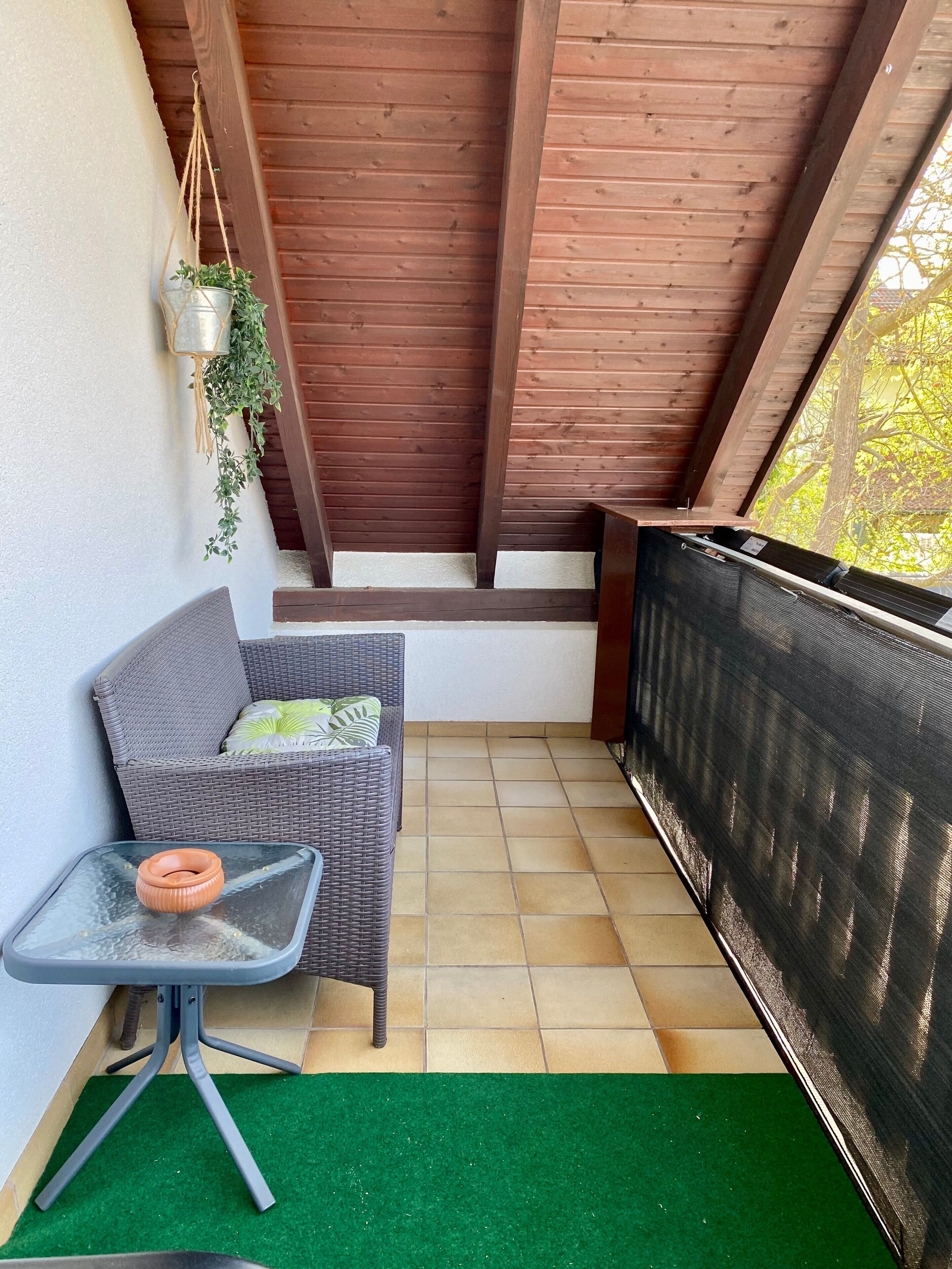 Een balkon met een rieten bank, een bijzettafeltje en een hangplant.