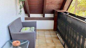 Een balkon met een rieten bank, een bijzettafeltje en een hangplant.