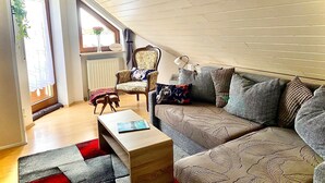 A cozy living room with a wooden ceiling, a sofa, a chair, a small table, and a window with a view. - Apartment 'Bassd Scho' with Shared Garden, Balcony and Wi-Fi (Ebensfeld)