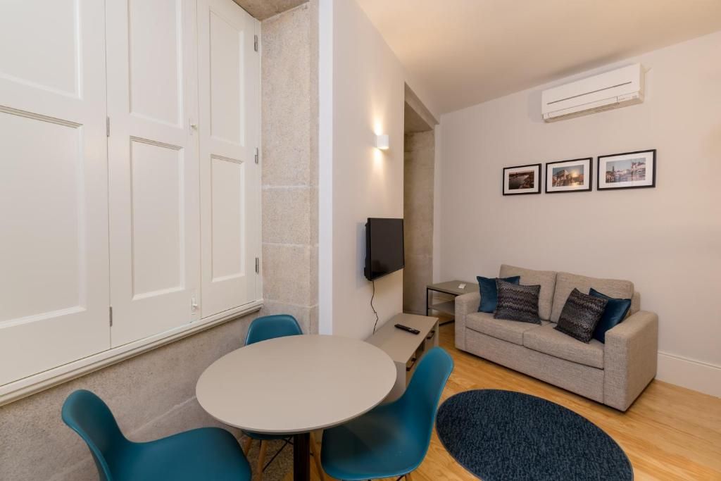 A room with a round table, blue chairs, a grey sofa, and a TV.