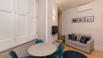 A room with a round table, blue chairs, a grey sofa, and a TV.