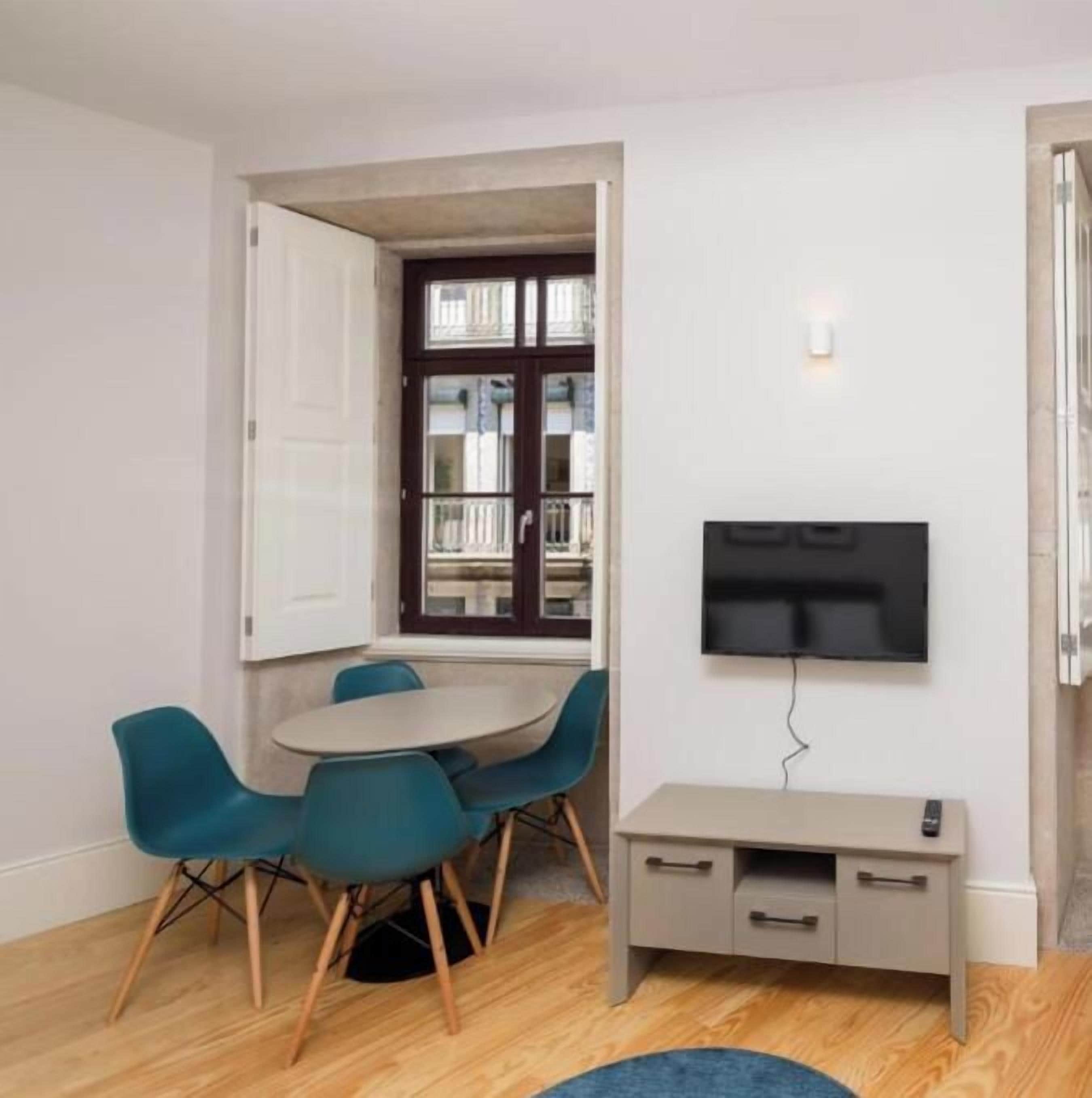 Un espacio habitable compacto con comedor, televisor montado en la pared y un mueble auxiliar.
